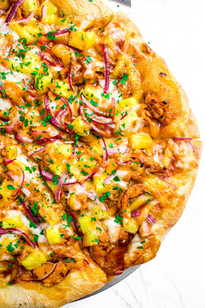 Overhead view of half a sliced barbecue pizza with soy curl chicken and red onions
