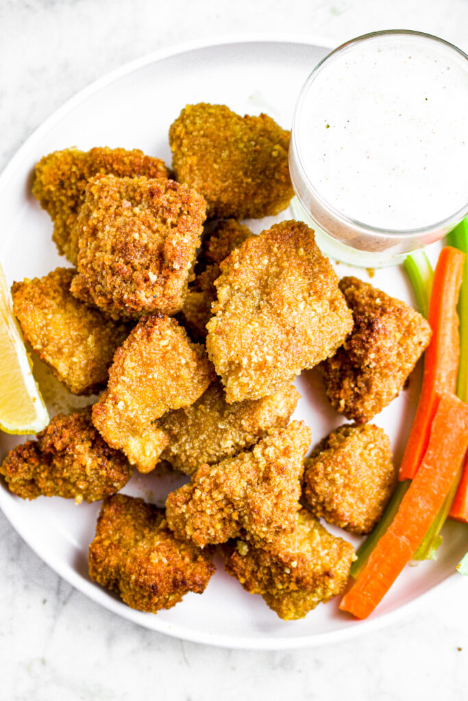 Overhead view of lemon pepper tofu wings on a round white plate with ranch dipping sauce in the top right corner