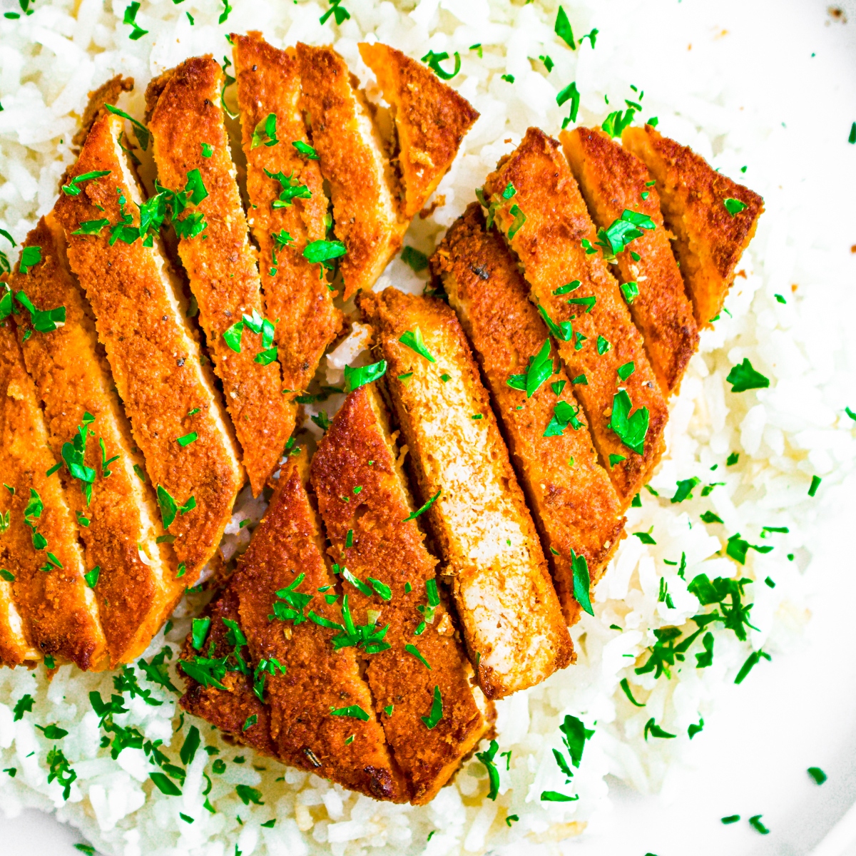 Overhead view of a red curry tofu cutlet sliced on a bias sitting on a bed of basmati rice sprinkled with parsley