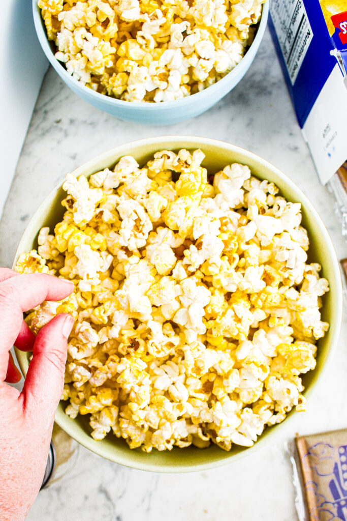 Overhead photo of a bowl of popcorn with a hand reaching in to pick up a piece
